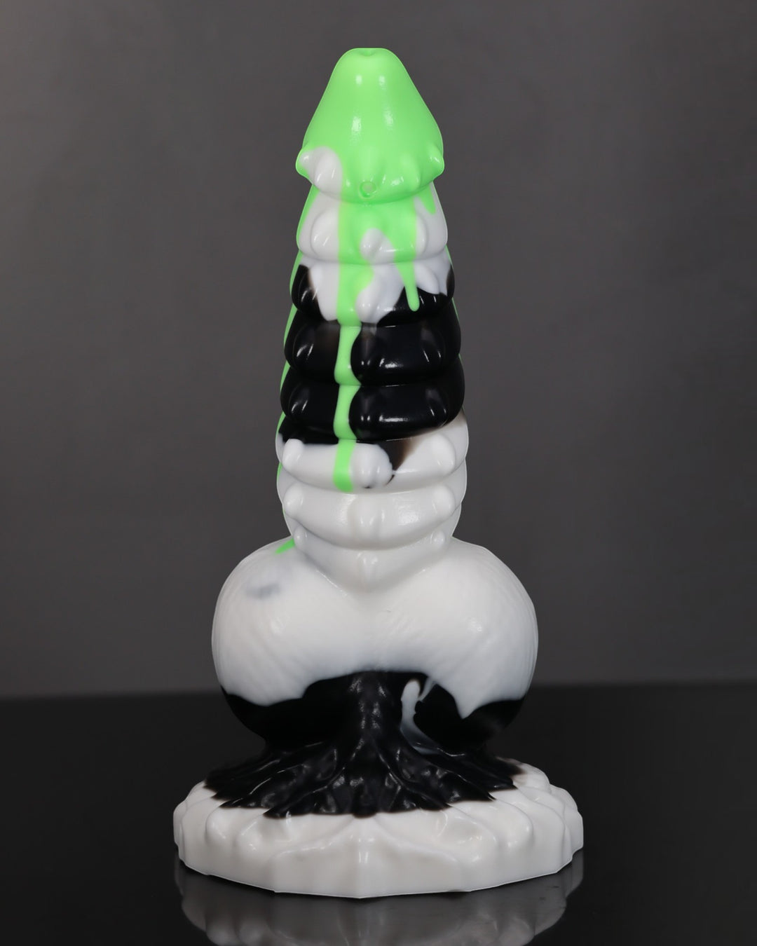 A novelty object with a stacked, melting look, featuring bright green dripping on top, white and black sections, and a white base, photographed against a dark gray studio background.