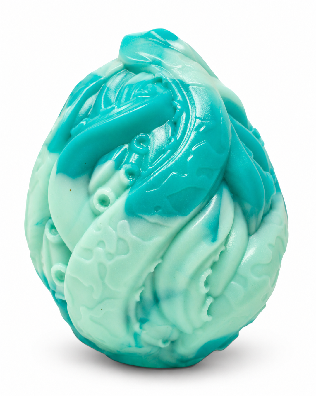 Turquoise and pale mint silicone egg with sculpted swirling ridges and circular details, on a white background with a soft shadow.