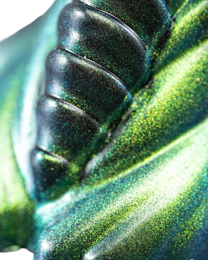 Close-up of overlapping sculpted plates showing the metallic teal and green shimmer of a Phreak silicone toy.